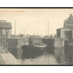 Prentbriefkaart uit 1910 met rechts Nieuwendijk 1. Een dekschuit met vaten maakt de krappe bocht naar de Brouwersgracht. Foto: Stadsarchief Amsterdam.