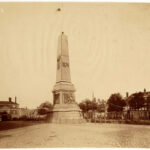 De gedenknaald op het Kadijksplein ter ere van het 25-jarig jubileum van Willem III anno 1874. Op de achtergrond het Poortgebouw van het Entrepotdok en de voorloper van de huidige Scharrebiersluis. Foto: Pieter Oosterhuis, Stadsarchief Amsterdam