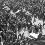 De pantserwagens van de Polar Bears en Duitse trucks passeren elkaar rakelings op de Dam dwars door de feestvierende menigte: een gespannen situatie. Foto via Stichting Memorial voor Damslachtoffers 7 mei 1945